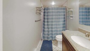 A bathroom with a shower curtain, toilet, sink, and mirror. - Comfortable ocean-view studio with pool (Ocean City)