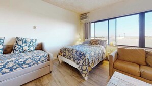 A bedroom with two beds, a sofa, and a large window. - Comfortable ocean-view studio with pool (Ocean City)