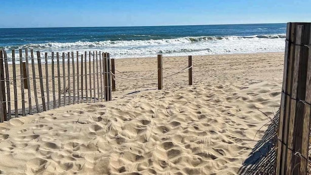 Ein Sandstrand mit einer Holzumzäunung und freiem Blick auf den Ozean.