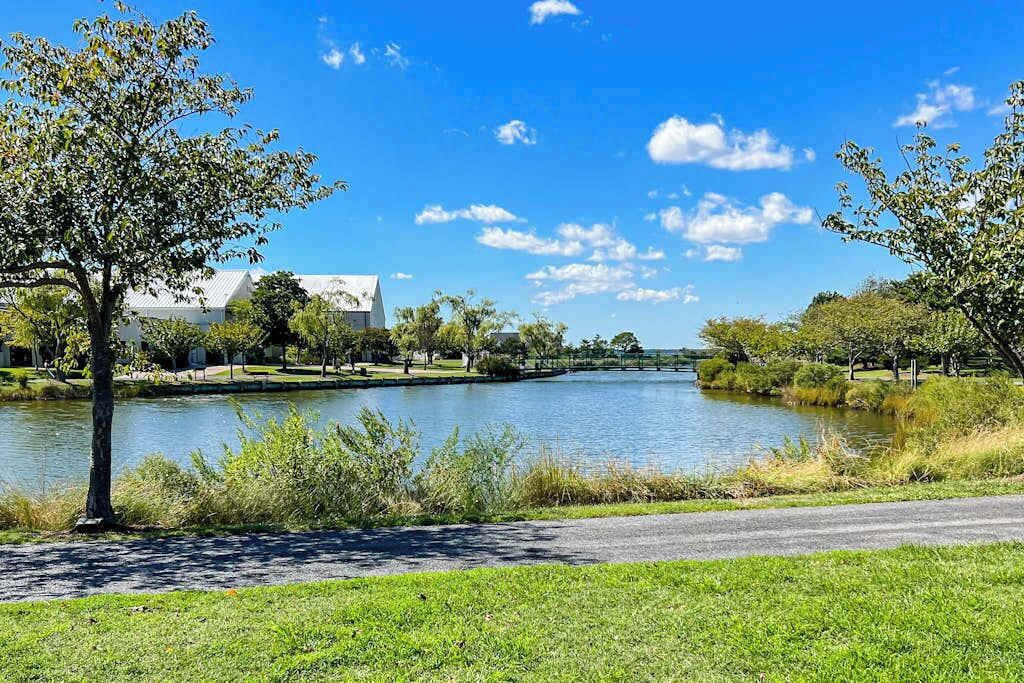 Un parc paisible au bord d’un lac, avec un sentier aménagé, des arbres et un bâtiment visible au loin.