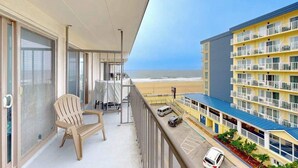 En balkon med en stol, et bord og udsigt til stranden og hotelbygningen.