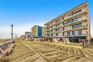A boardwalk with benches, a beachside building with multiple balconies, and a clear sky. - Decatur House 501 (Ocean City)