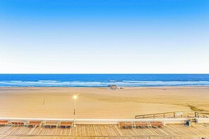 A beach view with a wooden boardwalk, lounge chairs, and a railing. - Decatur House 501 (Ocean City)