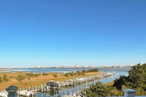 A marina with boats docked, a clear sky, and a distant cityscape. - The Sand Bar at Seaside Village (West Ocean City)
