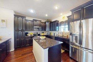 A modern kitchen with dark cabinetry, stainless steel appliances, and a granite island. - The Sand Bar at Seaside Village (West Ocean City)