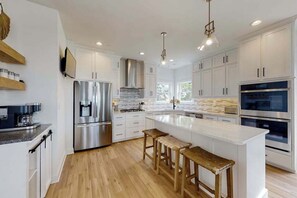 A modern kitchen with white cabinets, stainless steel appliances, wooden stools, and pendant lighting. - Sapphire Sol | House in Ocean City with elevator, roof deck, grill, streaming (Ocean City)