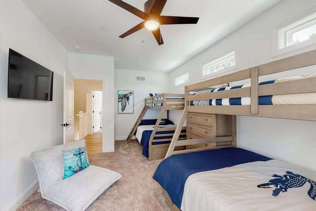 A bedroom with bunk beds, a ceiling fan, a TV, and a door leading to another room.