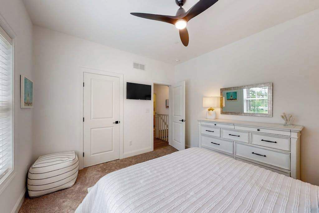 A bedroom with a bed, a ceiling fan, a dresser, and a television on the wall.