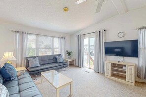 A living room with a sofa, coffee table, TV, and curtains. - Assateague Pointe - Helmsman (Berlin)