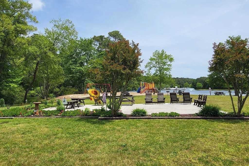 A park with picnic tables, a playground, and a lake view.