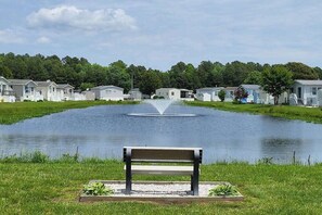 A bench by a pond with houses in the background. - Assateague Pointe - Helmsman (Berlin)