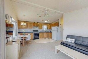 A compact kitchen with wooden cabinets, a dining table with chairs, a refrigerator, and a ceiling fan. - Assateague Pointe - Helmsman (Berlin)