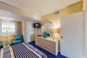 Ein Hotelzimmer mit Bett, Kommode, Fernseher und einem Fenster mit Vorhängen.