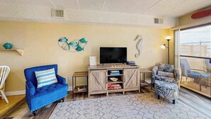 Un salon avec un canapé bleu, un fauteuil à motifs, un téléviseur posé sur un meuble en bois et une décoration représentant un hippocampe accrochée au mur.