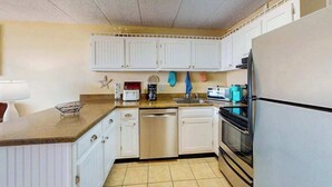 Une cuisine avec des meubles blancs, un lave-vaisselle, une cuisinière et un réfrigérateur.