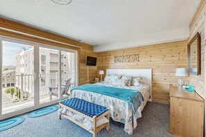 Un dormitorio con cama, un banco, un televisor y un balcón con vistas a edificios.