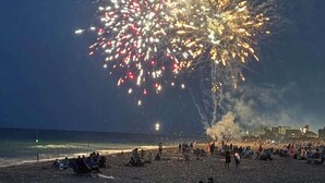 Een strand met mensen, een gebouw op de achtergrond en vuurwerk aan de hemel.