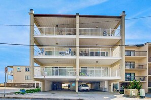 Un edificio de varios pisos con balcones, un garaje para estacionar y un cielo despejado.