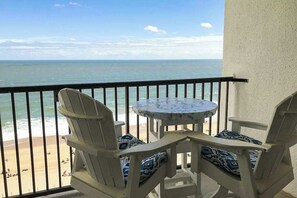 A balcony with a view of the beach, two chairs, and a small round table. - Oceanfront condo with a furnished balcony, central AC, washer/dryer, & pool (Ocean City)