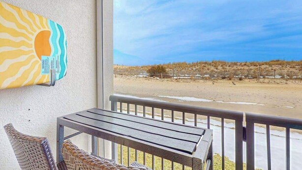 A balcony with a view of the beach, a wicker chair, and a wooden table. - Breakaway East 107 (Ocean City)
