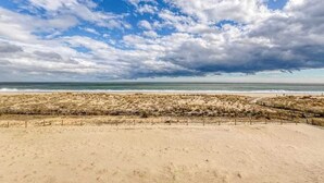 A beach with a sandy foreground and a grassy dune area. - Breakaway East 107 (Ocean City)