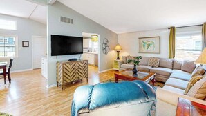 A living room with a sofa, a television, a coffee table, and a dining area with a table and chairs. - Bayside Keys 627 (Ocean City)
