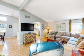 Ein Wohnzimmer mit einer Couch, einem Fernseher, einem Couchtisch und einem Essbereich mit Tisch und Stühlen.