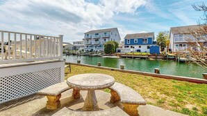 A waterfront property with a dining area, a white fence, and buildings in the background. - Bayside Keys 627 (Ocean City)
