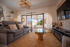 Ein modernes Wohnzimmer mit einem grauen Sofa, einem Glastisch und einem an der Wand befestigten Fernseher.