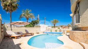 A swimming pool with lounge chairs, palm trees, and a stone wall. - CostaBlancaDreams - Casa Kaiyo in Calpe (Calpe / Calp)
