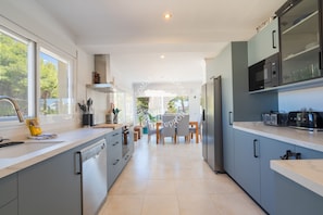 A modern kitchen with grey cabinets, a dishwasher, a microwave, and a dining area with chairs and a table. - CostaBlancaDreams - Villa Mar y Monte in Calpe (Calpe / Calp)
