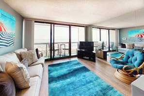 A modern living room with a sofa, a blue rug, a television, and a chair. - Oceanfront condo with a balcony, central AC, pools, game room & sports courts (Ocean City)