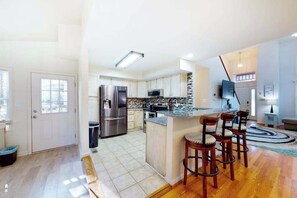 A modern kitchen with a central island, stainless steel appliances, and a bar area with stools. - 5 Whitecap (Ocean Pines)