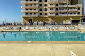 A swimming pool with lounge chairs and umbrellas, a multi-story building with balconies, and a clear sky. - 5 Whitecap (Ocean Pines)