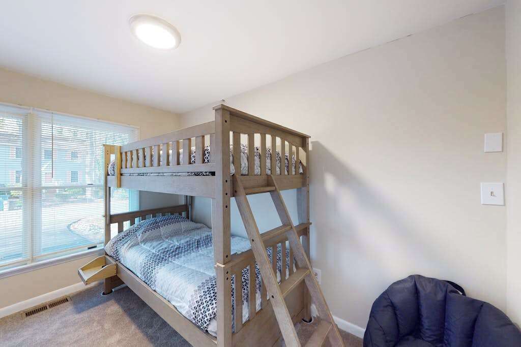 Een stapelbed in een kamer met een raam, een stoel en een lichtschakelaar aan de muur.