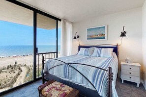Ein Schlafzimmer mit Bett, Nachttisch, Lampe, Gemälde und Blick auf den Strand.