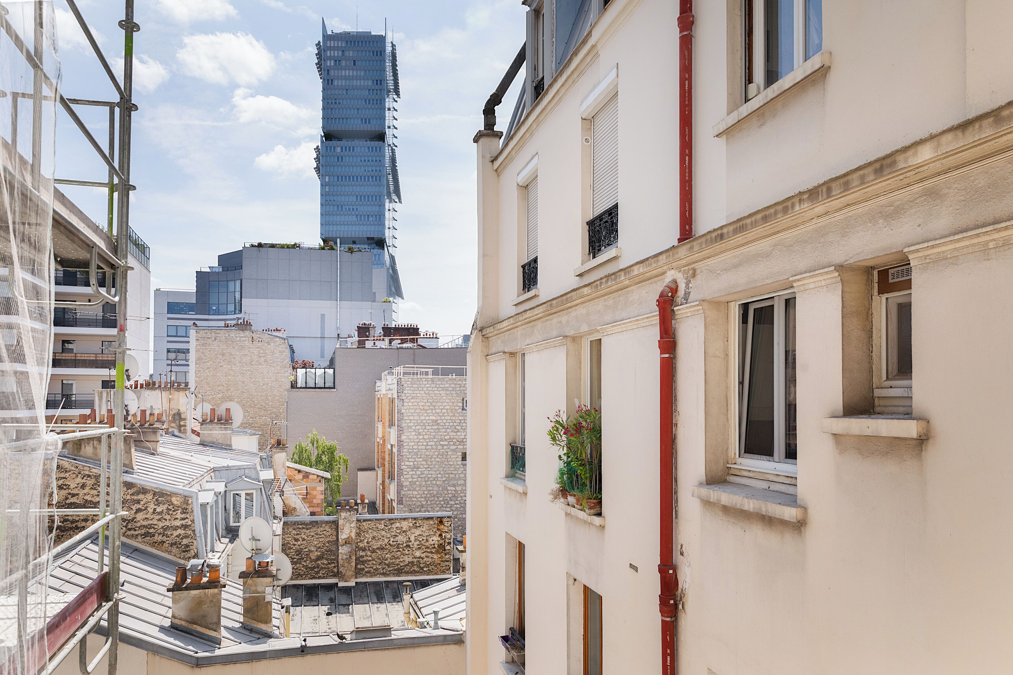 Un paisaje urbano con un rascacielos moderno, edificios tradicionales y una azotea con andamios de construcción.