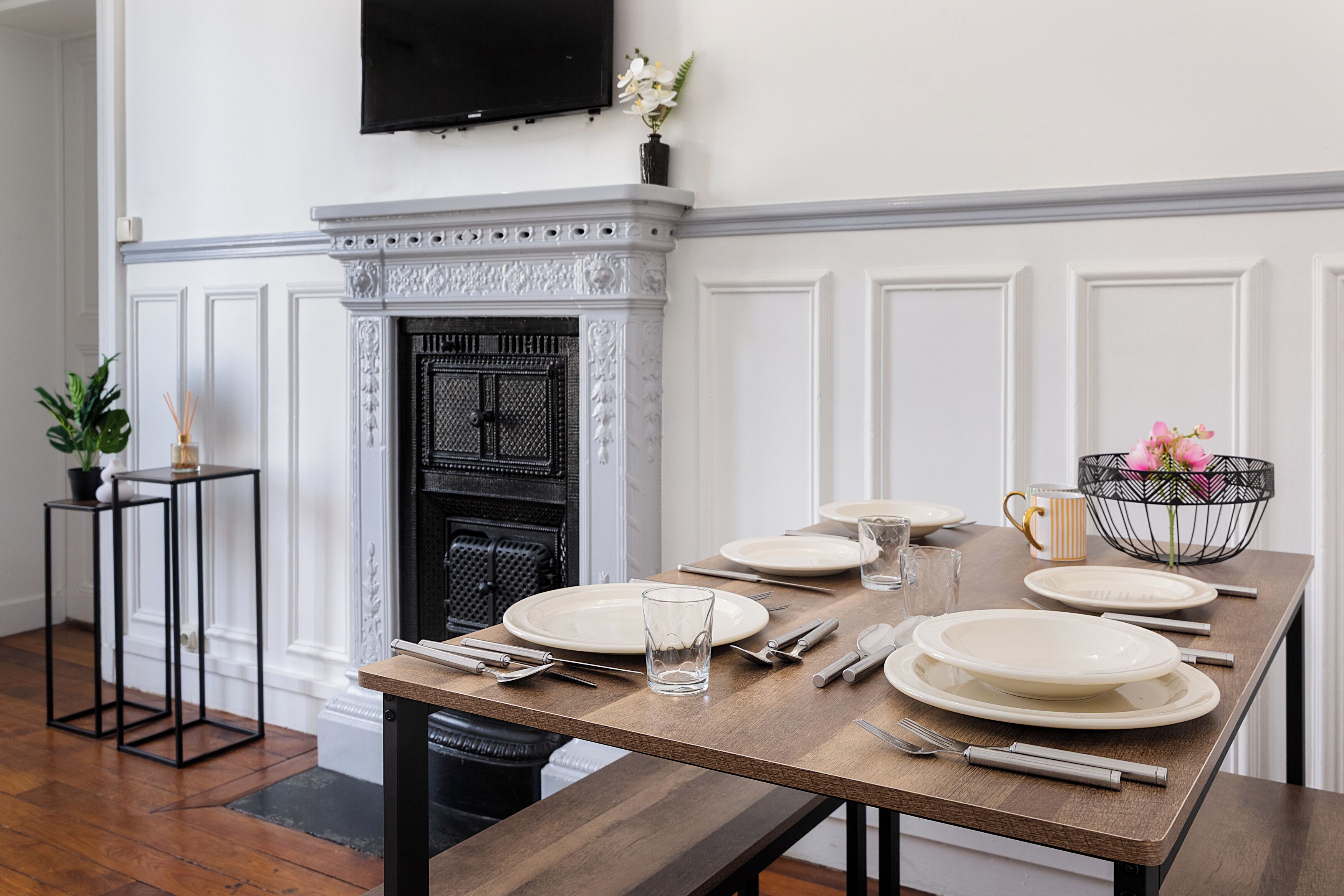 A dining table set with plates, glasses, and cutlery, a fireplace, and a television mounted on the wall.