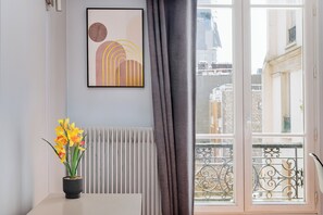 A room with a radiator, a potted plant, a framed artwork, and a view of buildings through a window with a balcony. - Parisian charm, separate beds, screen and work desk, ideal for families and professionals. (Clichy)