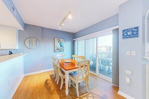 A dining area with a wooden table and chairs, a clock on the wall, and a view of the outside through large windows. - Dog-friendly water-view condo with rooftop pool, balcony, W/D, jetted tub (Ocean City)