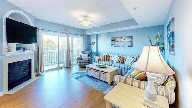 A living room with a fireplace, a television, a sofa, a coffee table, and a ceiling fan. - Captiva Bay 202 (Ocean City)