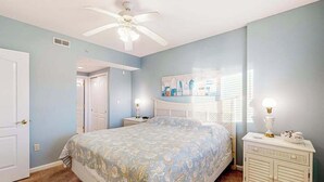 A bedroom with a bed, a nightstand, a dresser, a ceiling fan, and a door. - Captiva Bay 202 (Ocean City)