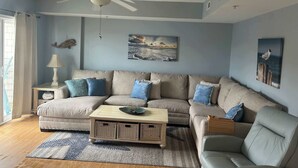 A living room with a sectional sofa, a ceiling fan, and wall art. - Captiva Bay 202 (Ocean City)