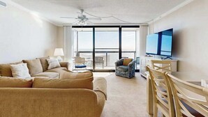 Ein Wohnzimmer mit einer Couch, Sesseln, einem Fernseher und einem Balkon mit Blick.