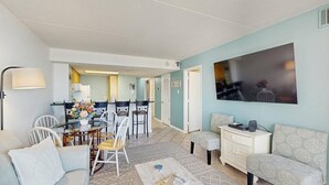 A living room with a sofa, a coffee table, and a dining area with chairs and a table. - Stunning oceanfront condo w/ private balcony, beach access, pools & game rooms (Ocean City)