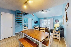 A dining area with a wooden table and benches, a staircase, a television, and a sign that reads 'BEACH HOUSE'. - Sunny condo w/balconies, full kitchen, A/C & Wifi & close to parks & the beach (Ocean City)