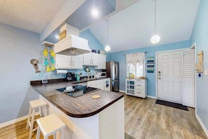 A modern kitchen with white cabinets, a central island with stools, a refrigerator, and a microwave. - Sunny condo w/balconies, full kitchen, A/C & Wifi & close to parks & the beach (Ocean City)