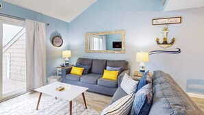 Ein Wohnzimmer mit grauem Sofa, zwei Beistelltischen mit Lampen, einem weißen Couchtisch, einem Spiegel und einer Wanddekoration als Anker.