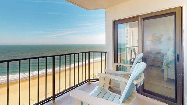Een balkon met uitzicht op strand en zee, een schuifpui en twee Adirondack-stoelen.