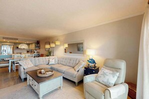 Un salon avec un canapé, une table basse, un fauteuil et, au fond, un coin cuisine.
